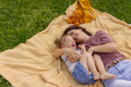 mother and daughter laughing as they lie down on a picnic blanket